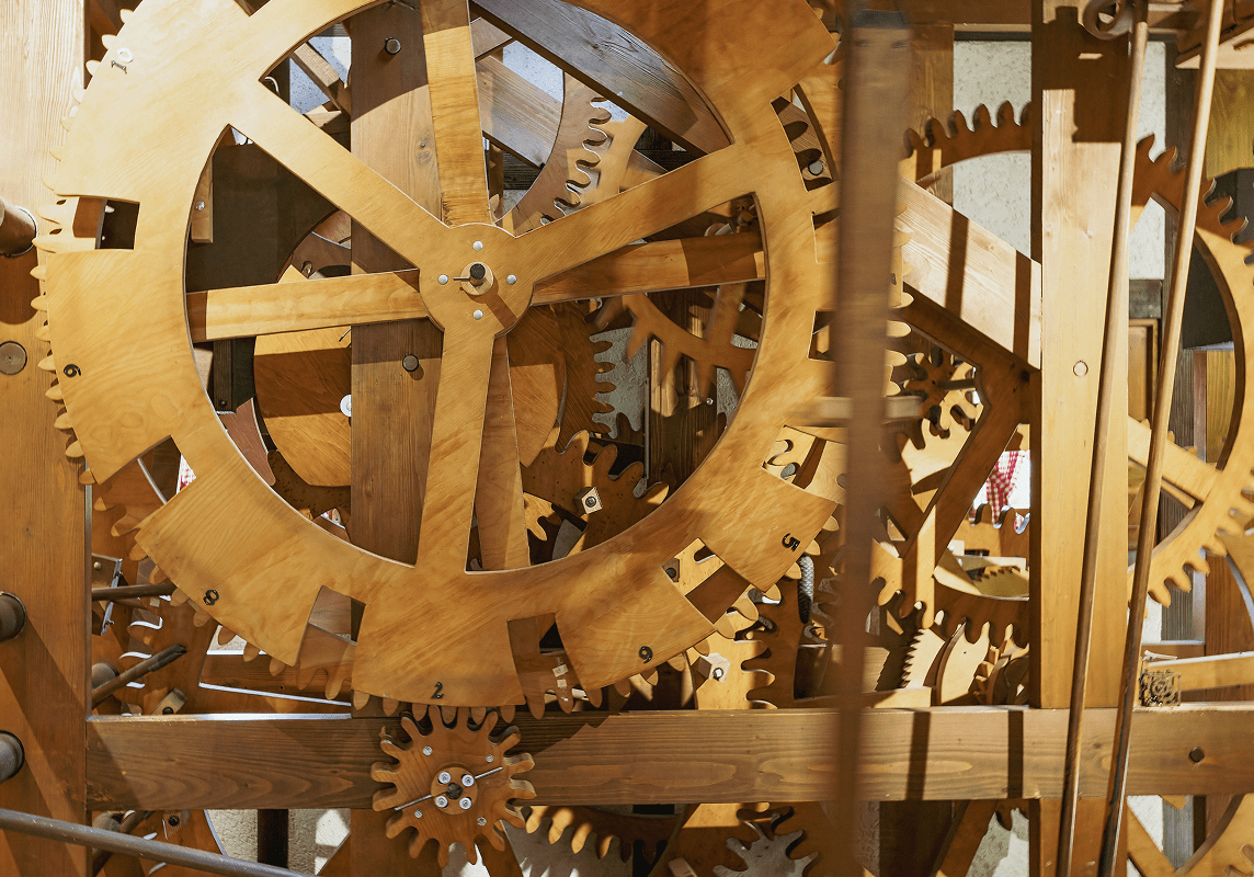 Close-up view of interlocking wooden gears and mechanisms inside a large mechanical clock or device.
